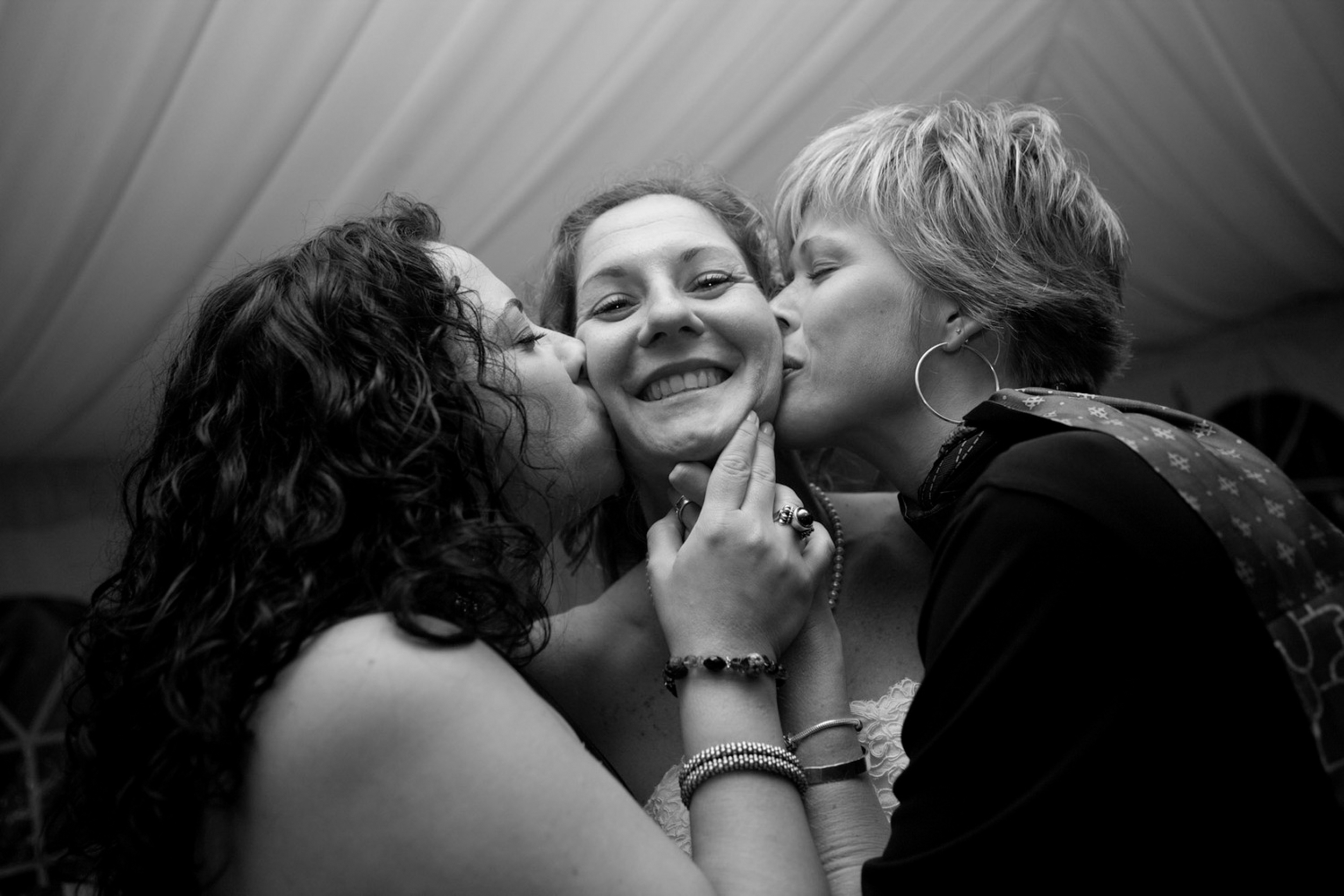 Two women kissing a smiling woman on each cheek in black and white.