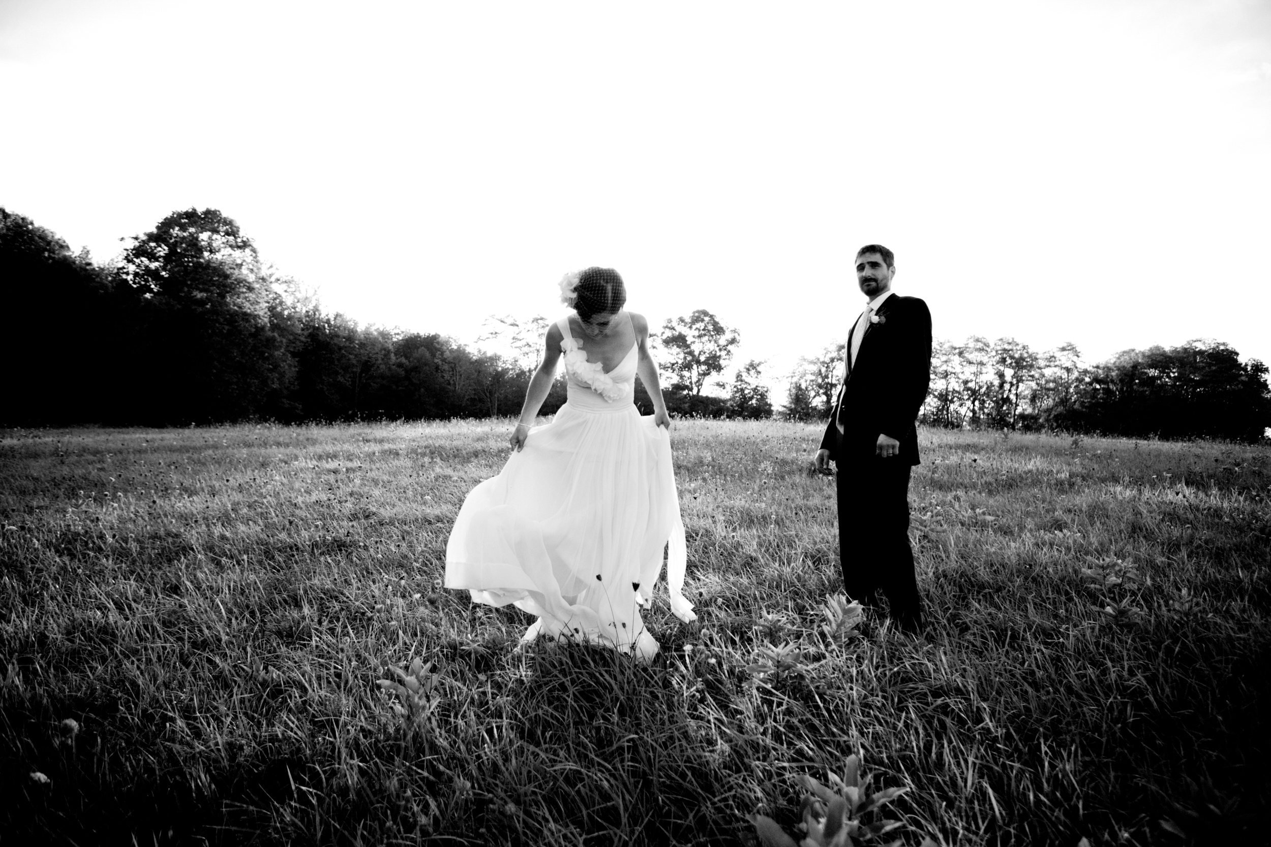 Bride and groom walking through a grassy field in black and white.