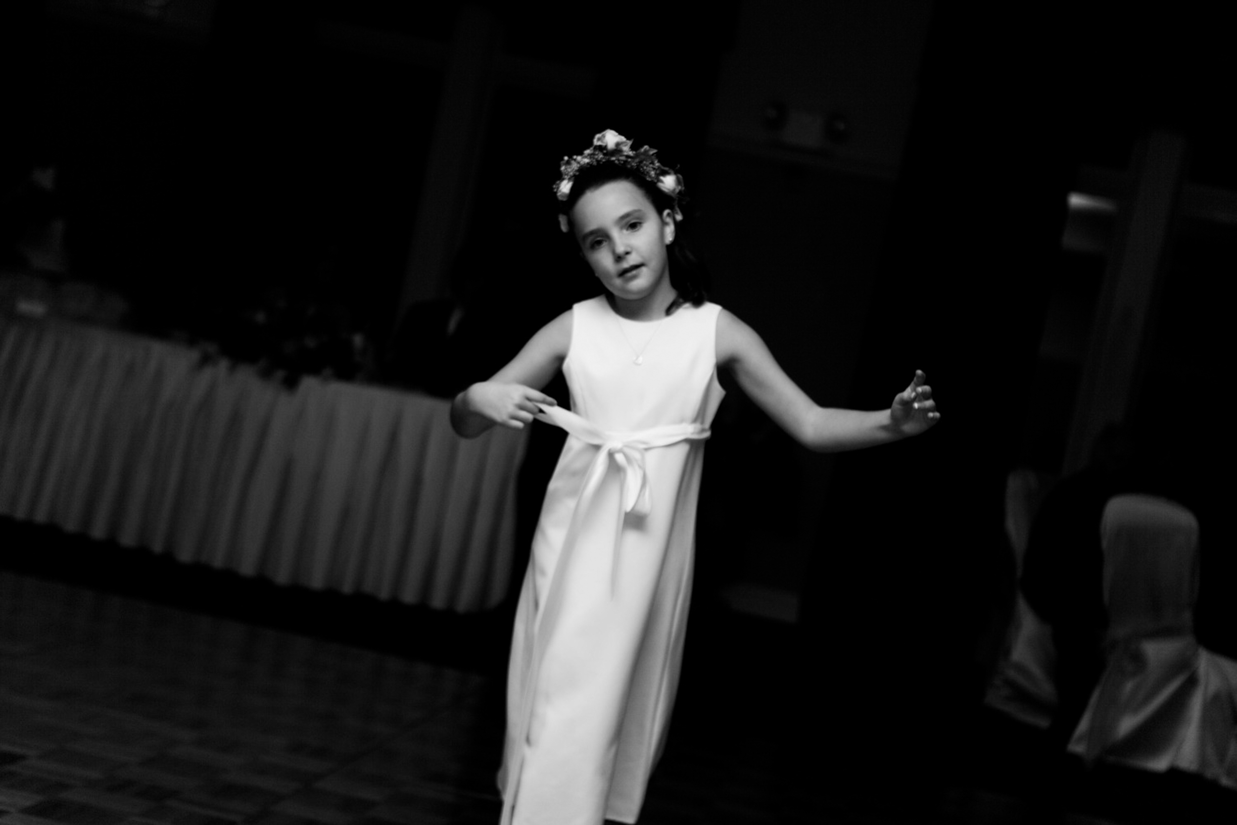 A young girl in a white dress and flower crown dances gracefully.