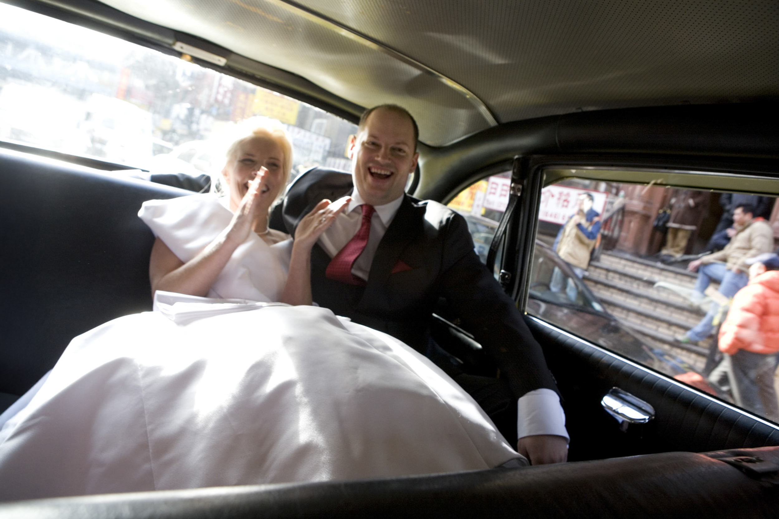Happy newlywed couple smiling inside a car on their wedding day.