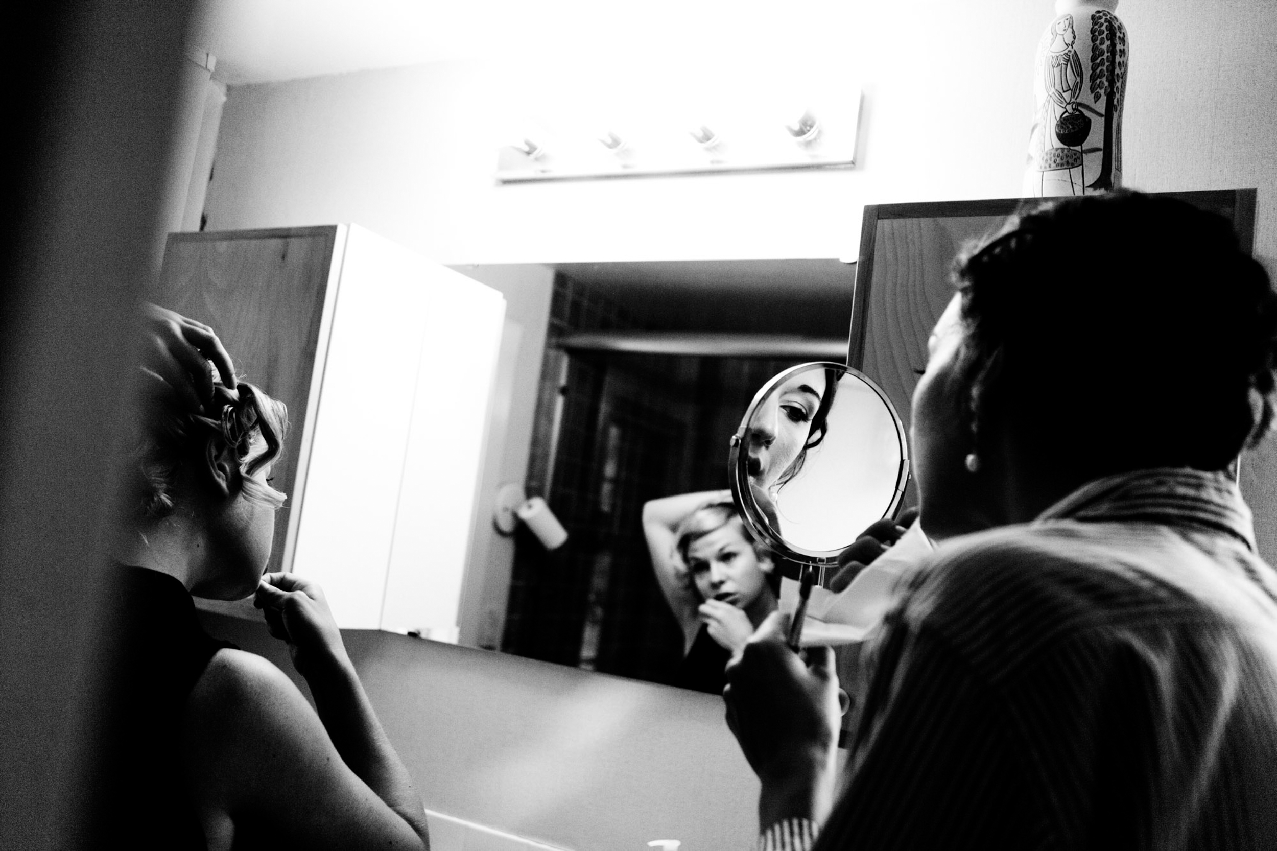 Person applying makeup in front of a mirror in black and white.