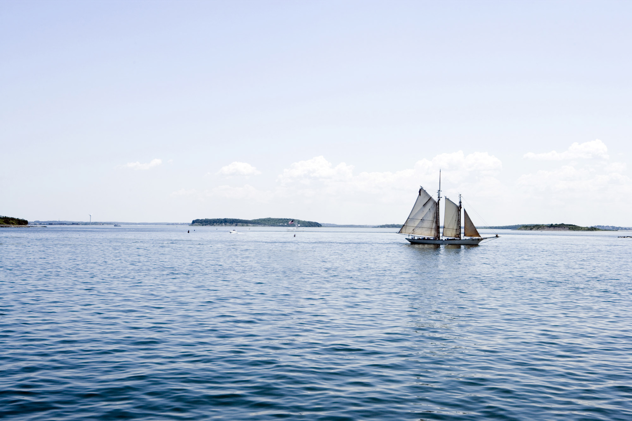 A sailboat glides across calm blue waters near a distant island.