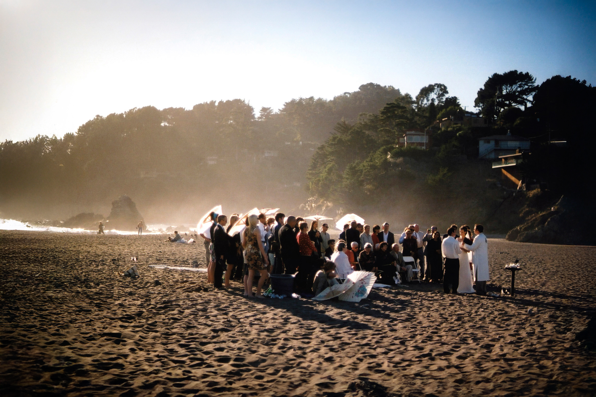 A group gathered on a foggy beach, possibly for a ceremony at sunrise.