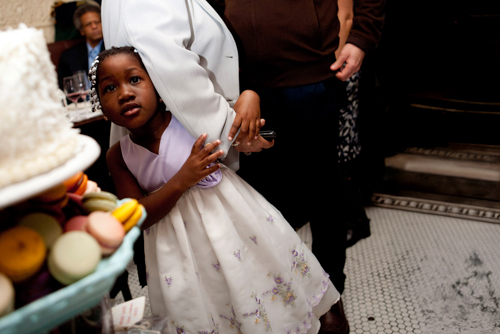 A young girl in a white dress holding an adult's hand, looking up anxiously.