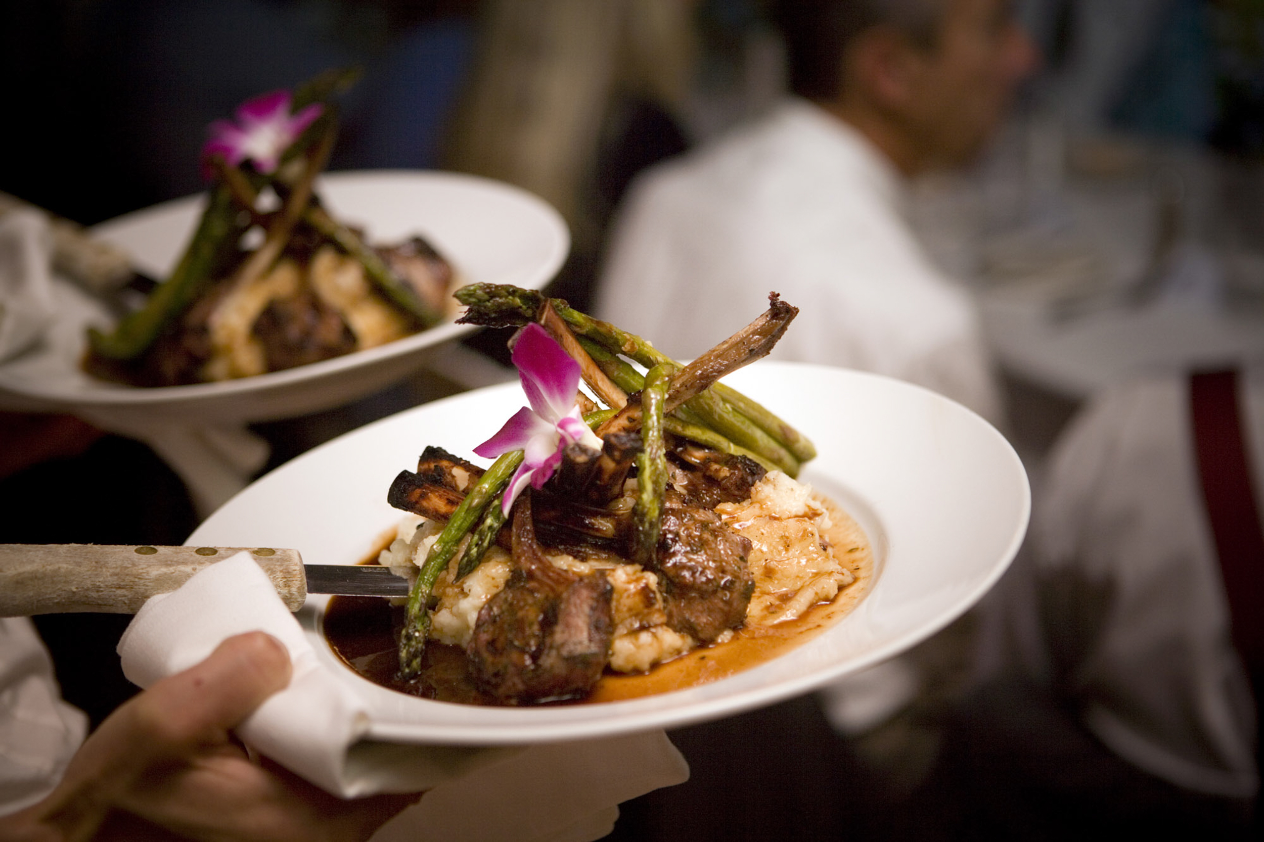 Gourmet dish with grilled meat and garnishes, served on a white plate.