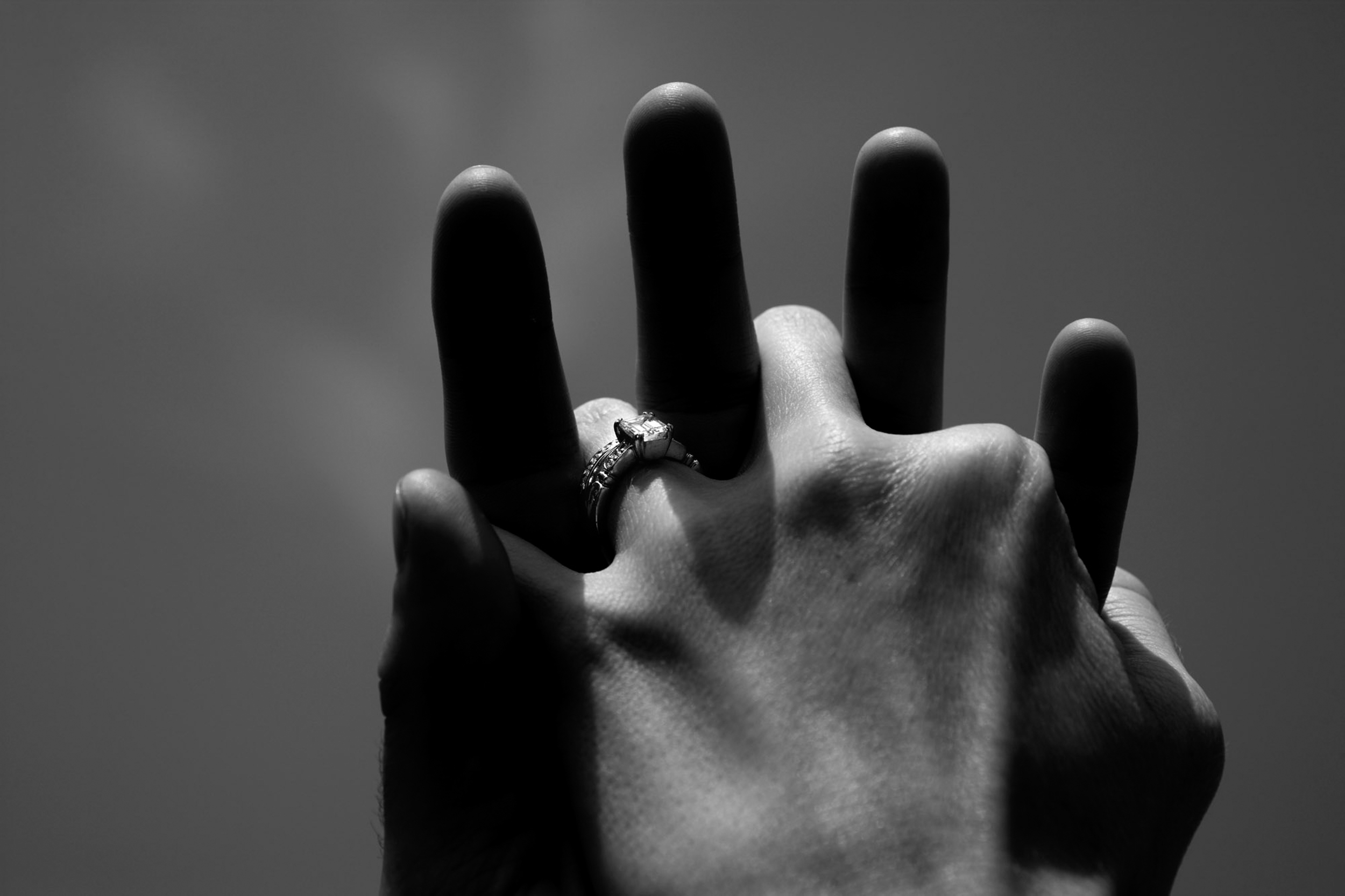 Two hands holding, one with an engagement ring, in black and white.