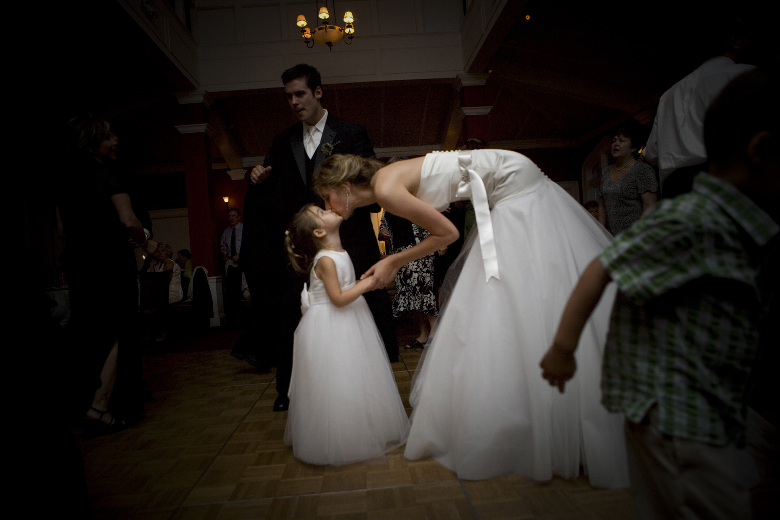 Bride bending down to kiss a young flower girl during a wedding.