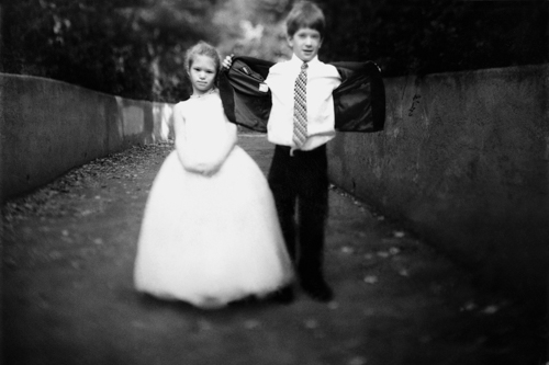 A young boy and girl dressed formally, standing outdoors on a path.