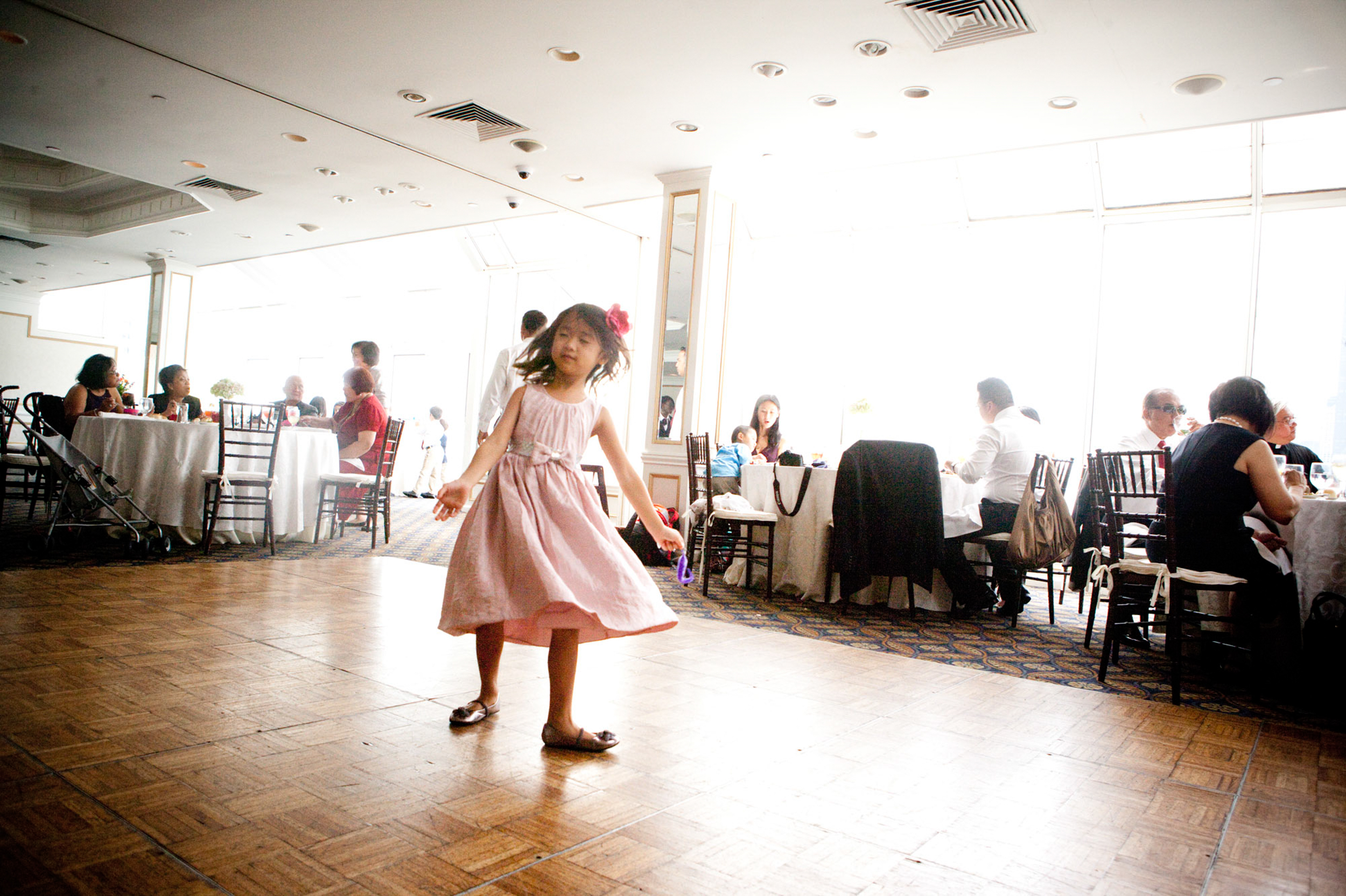 A young girl twirls joyfully on a wooden dance floor in a bright room.