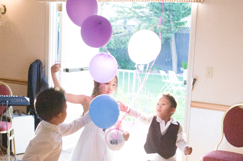 Children joyfully playing with colorful balloons indoors near a glass door.
