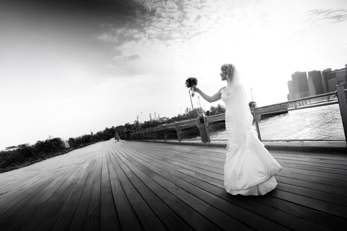Bride in a white gown holding a bouquet, walking on a wooden boardwalk.