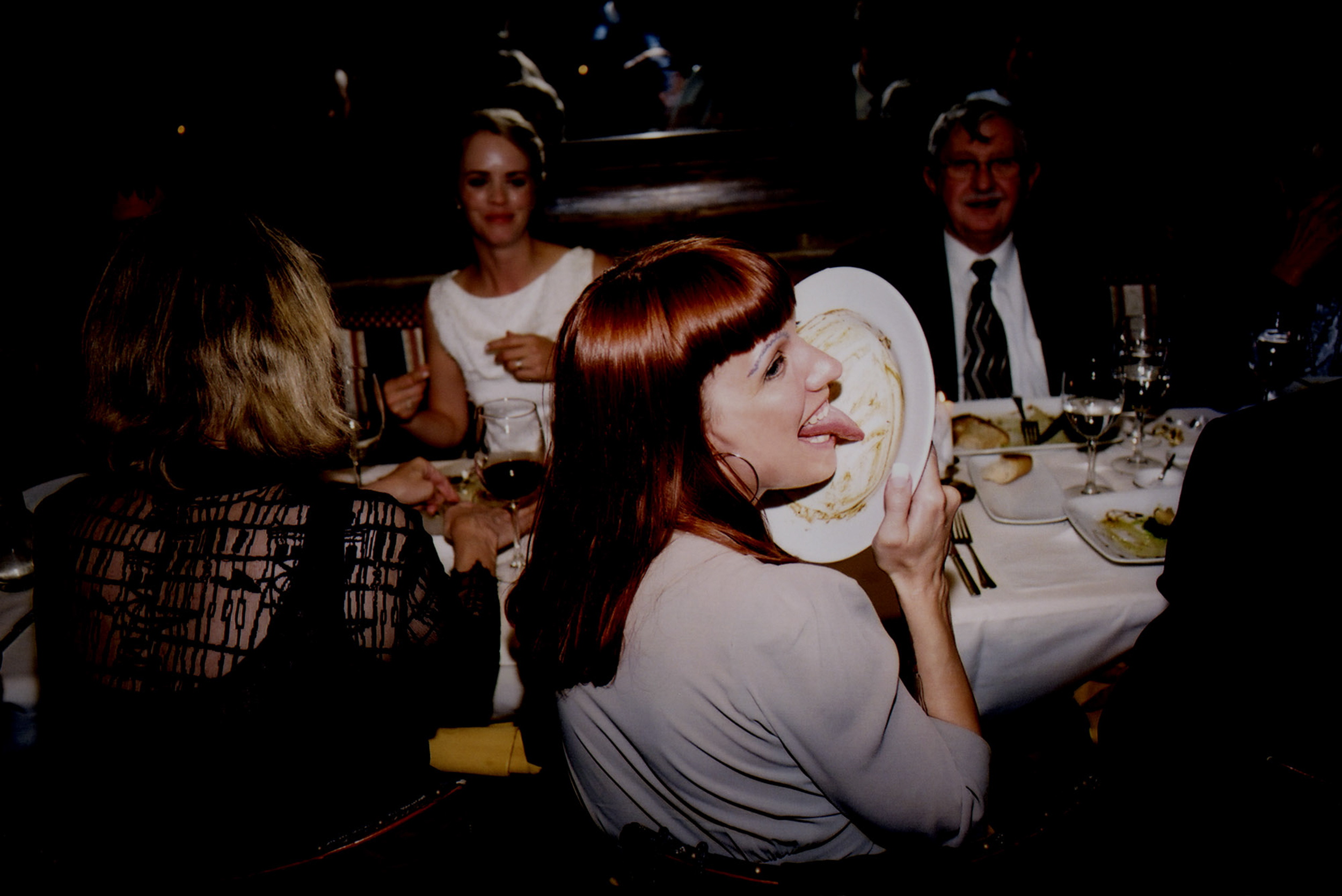 Woman playfully holding a pie to her face at a dinner table.