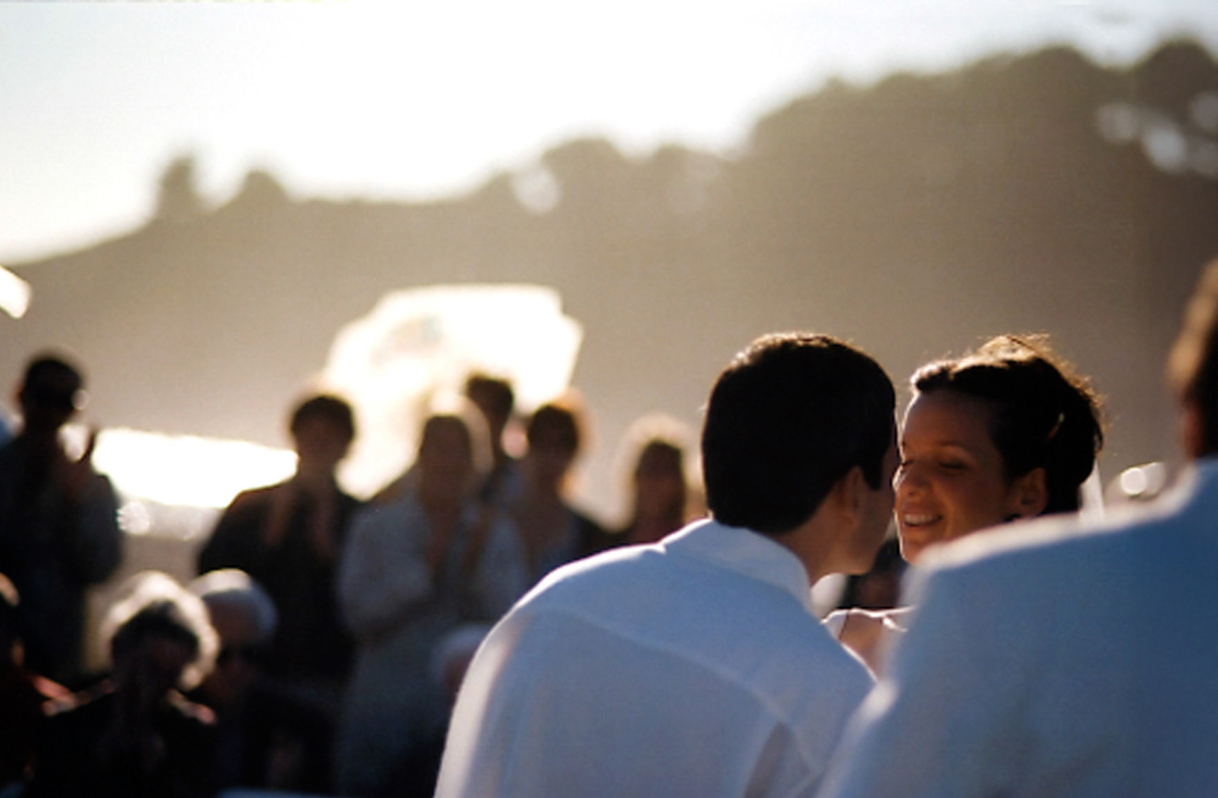 Couple sharing a close moment outdoors with blurred crowd in background.