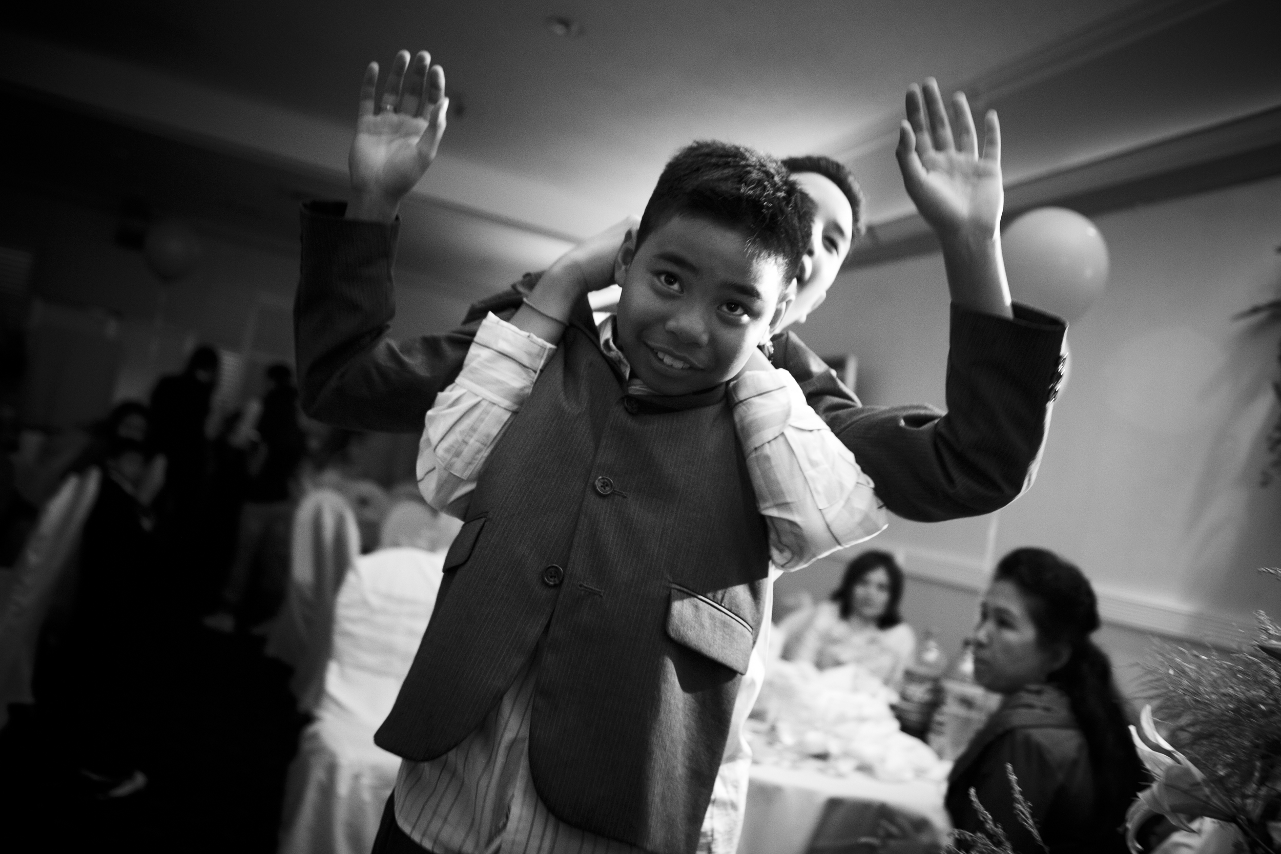 A joyful boy giving a piggyback ride to a younger child, both smiling and waving.