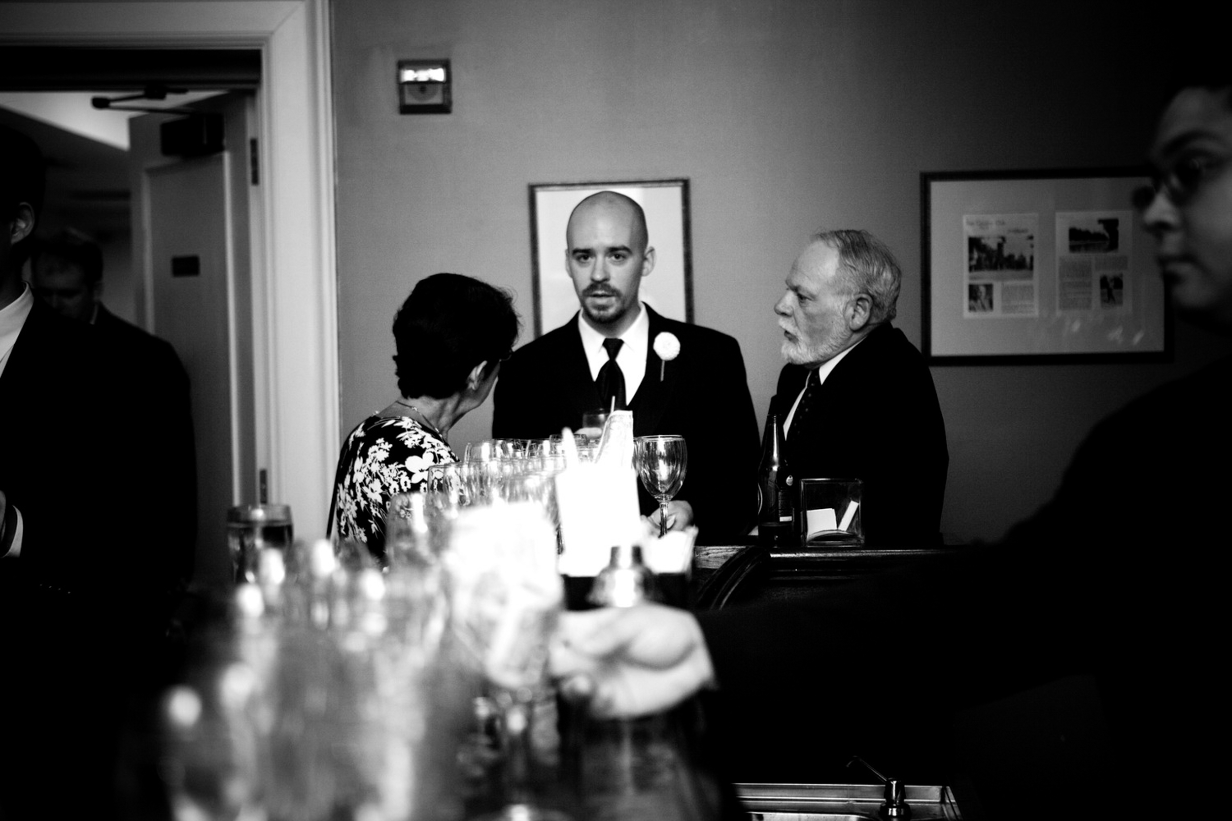 Three people socializing at a bar or reception area in black and white.