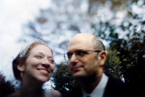 A smiling woman and a man in glasses with a blurred background.