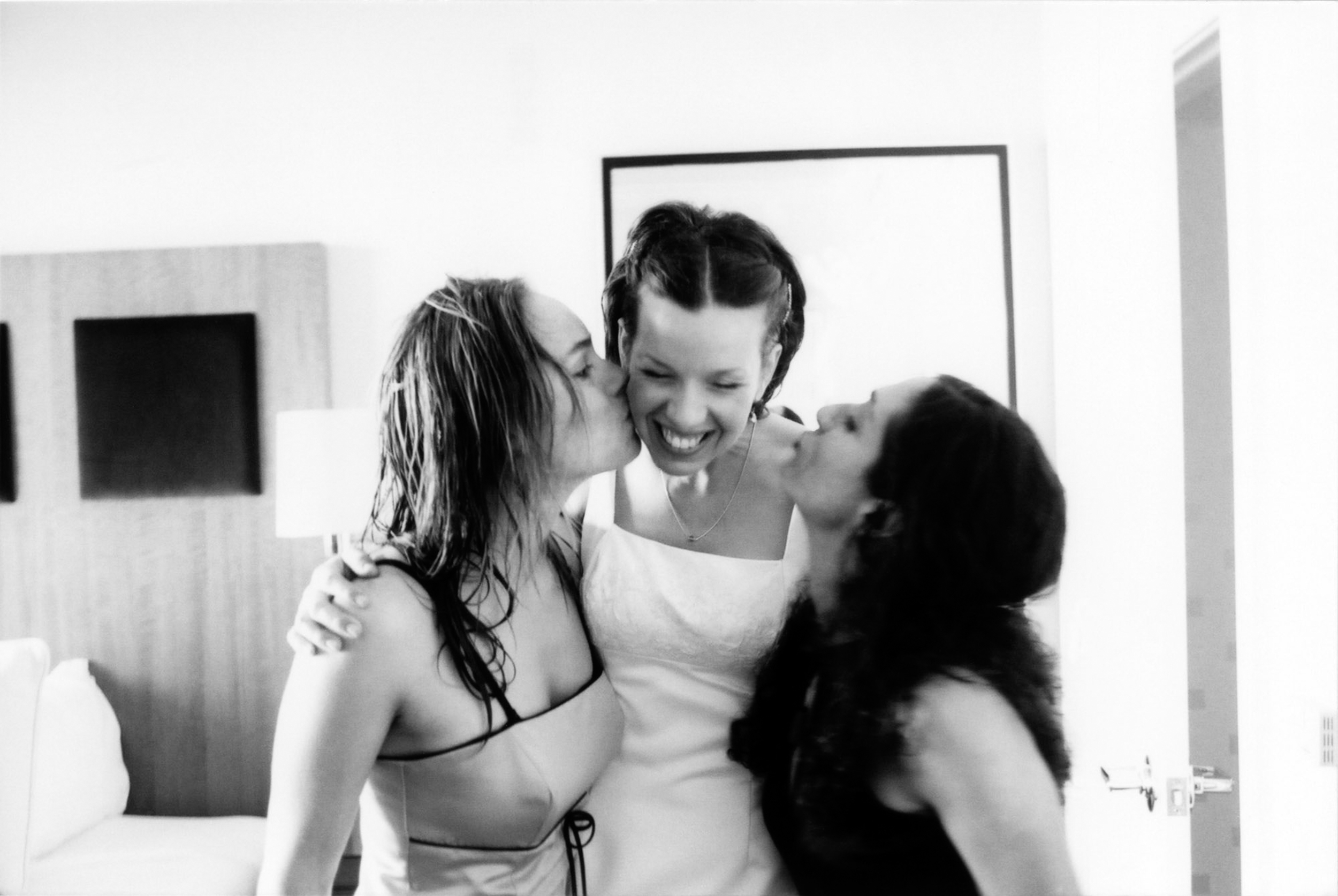 Two women kissing a young girl on the cheeks, all smiling joyfully.