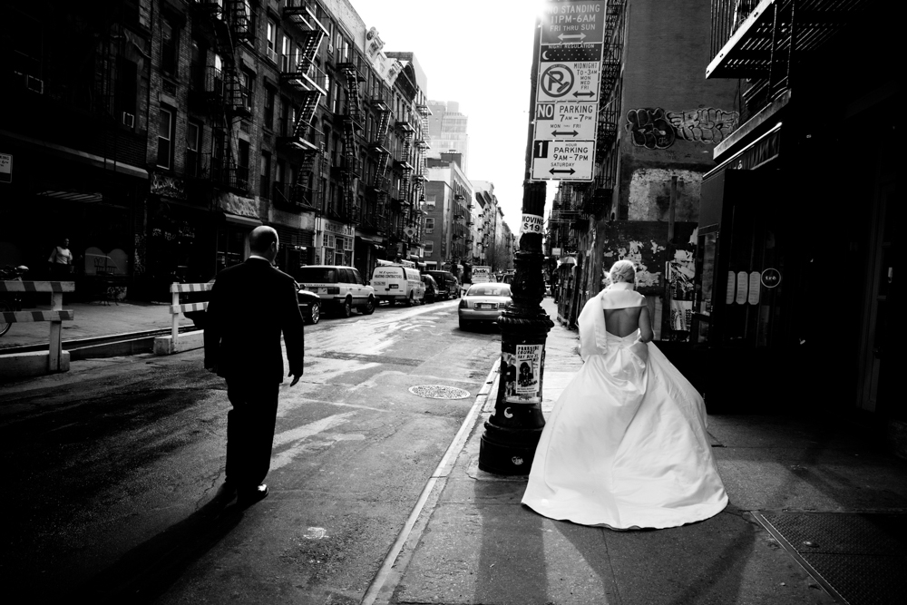 Bride in wedding dress on city street, man walking away.